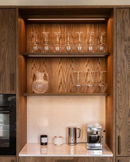 Elegant kjøkken i mørkt treverk med en lys benkeplate og backsplash i kompositt. Utført av Lomundal.