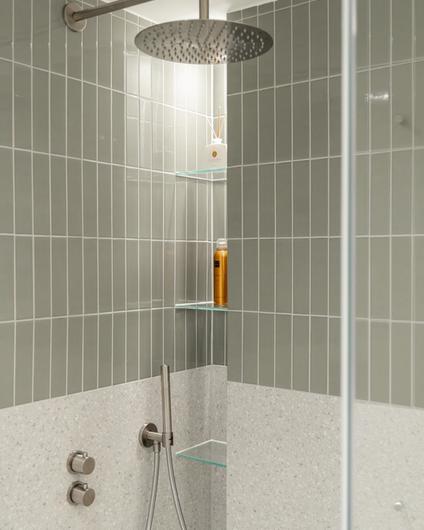 Dusjsone med blanke, smale fliser og terrazzofliser. Badet har et naturlig og skandinavisk preg i duse grønntoner. Utført av Lomundal.
