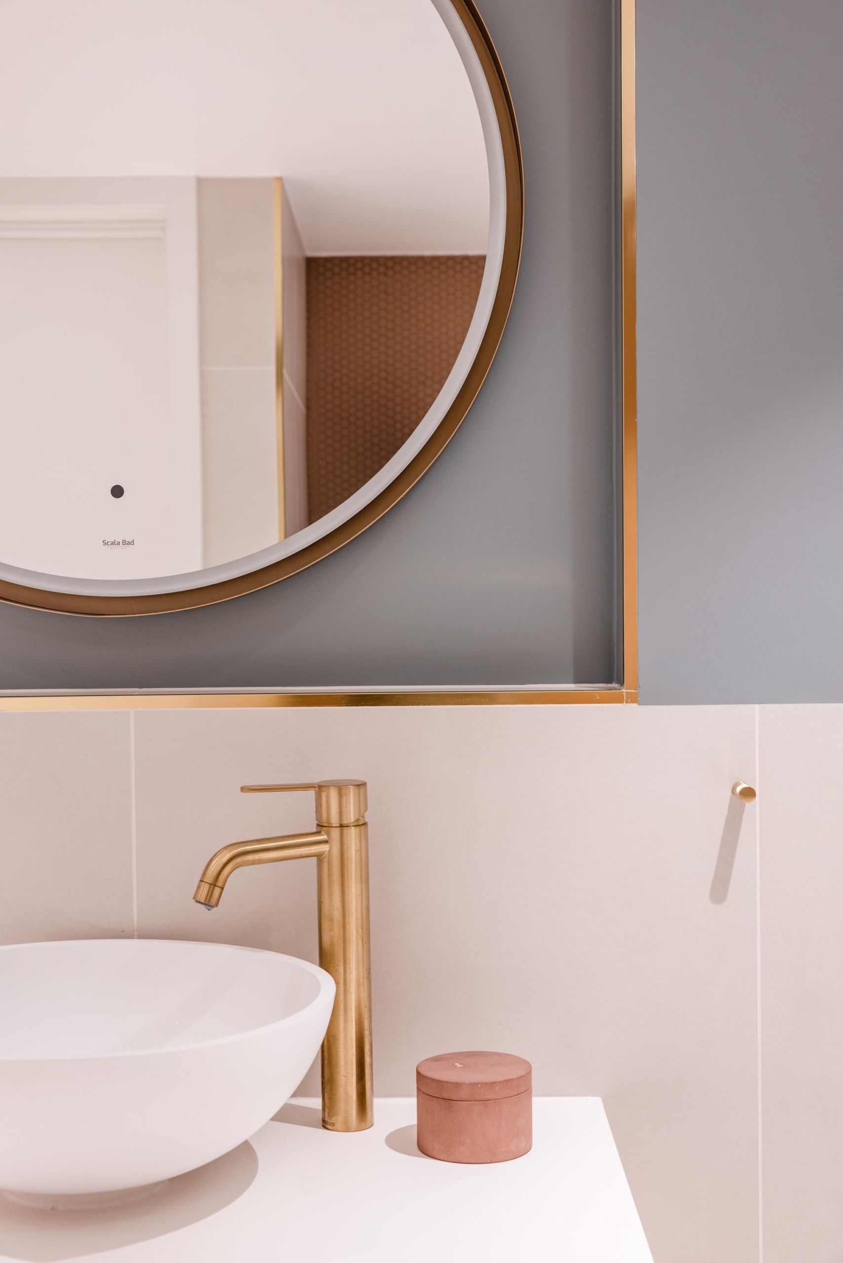 Detaljbilde fra baderom med beige fliser og blå malt vegg over vask. Armatur og andre detaljer i messing. Utført av Lomundal.