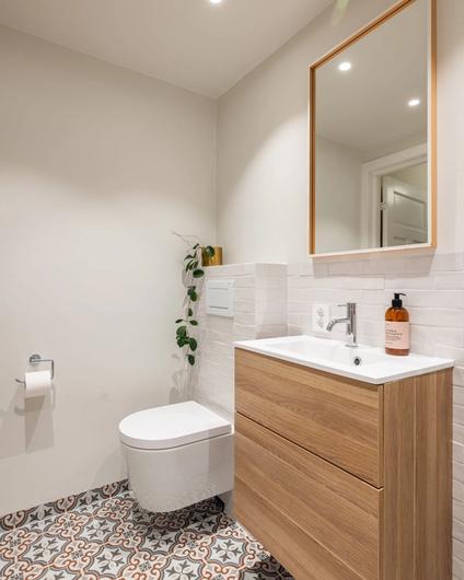 Vegghengt toalett og baderomsmøbel i tre, med hvite brick-fliser og mønsterflis på gulvet. Badet er totalrenovert av Lomundal.