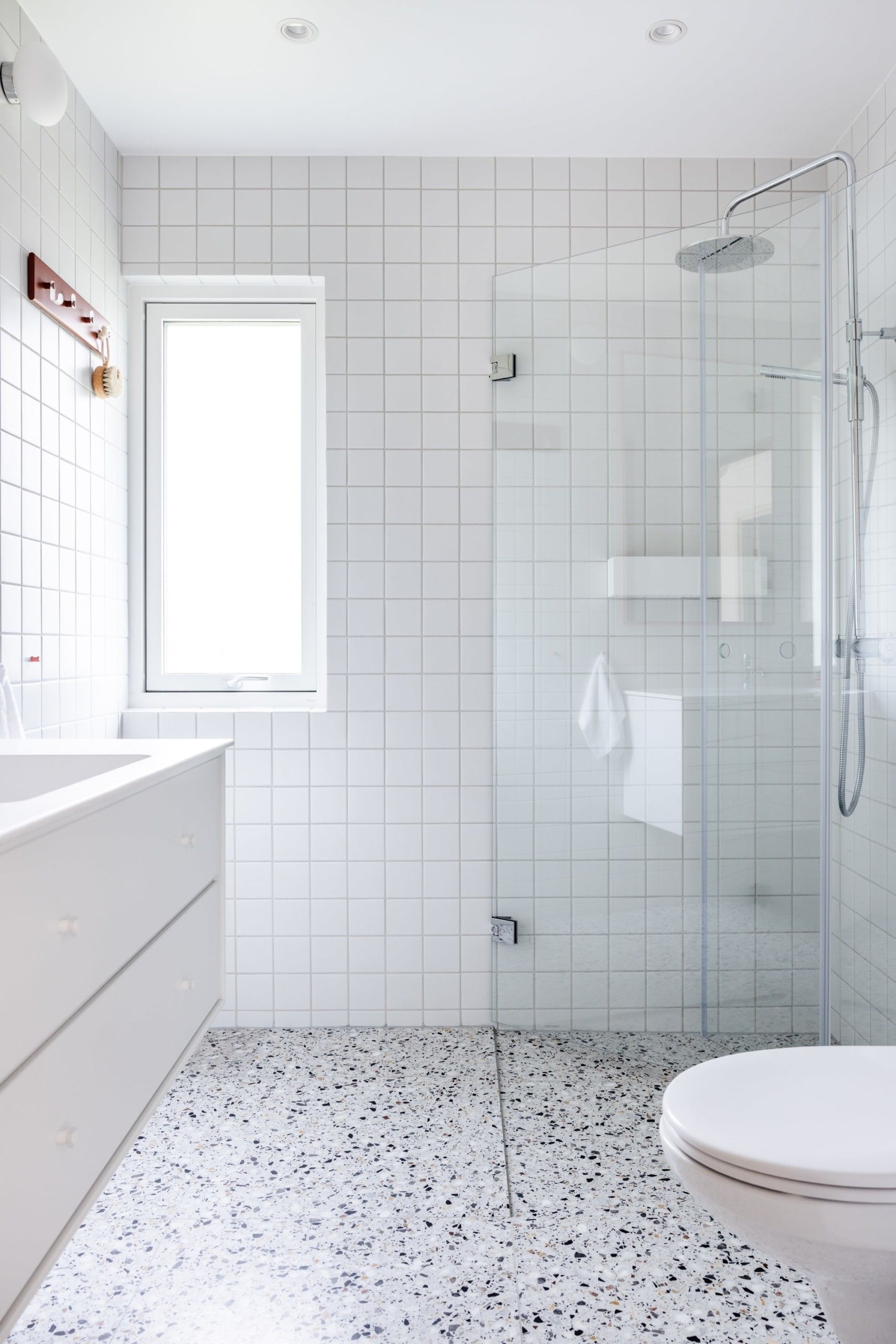 Retro bad med lys terrazzo flis på gulv og hvite kvadratiske fliser på vegg. Armaturer i krom og hvit baderomsinnredning fra Montana.