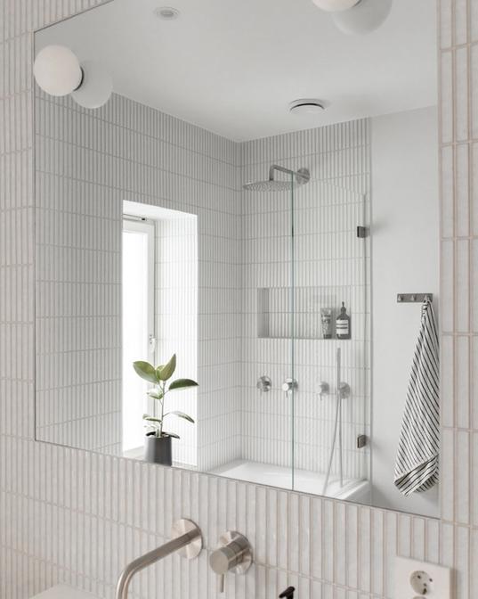 Lyst og moderne bad med avlang kitkat flis på vegg, innebygde armaturer i stål fra Qtoo. Badet har en enkel servant og badekar med dusj. Badet er pusset opp av Lomundal.