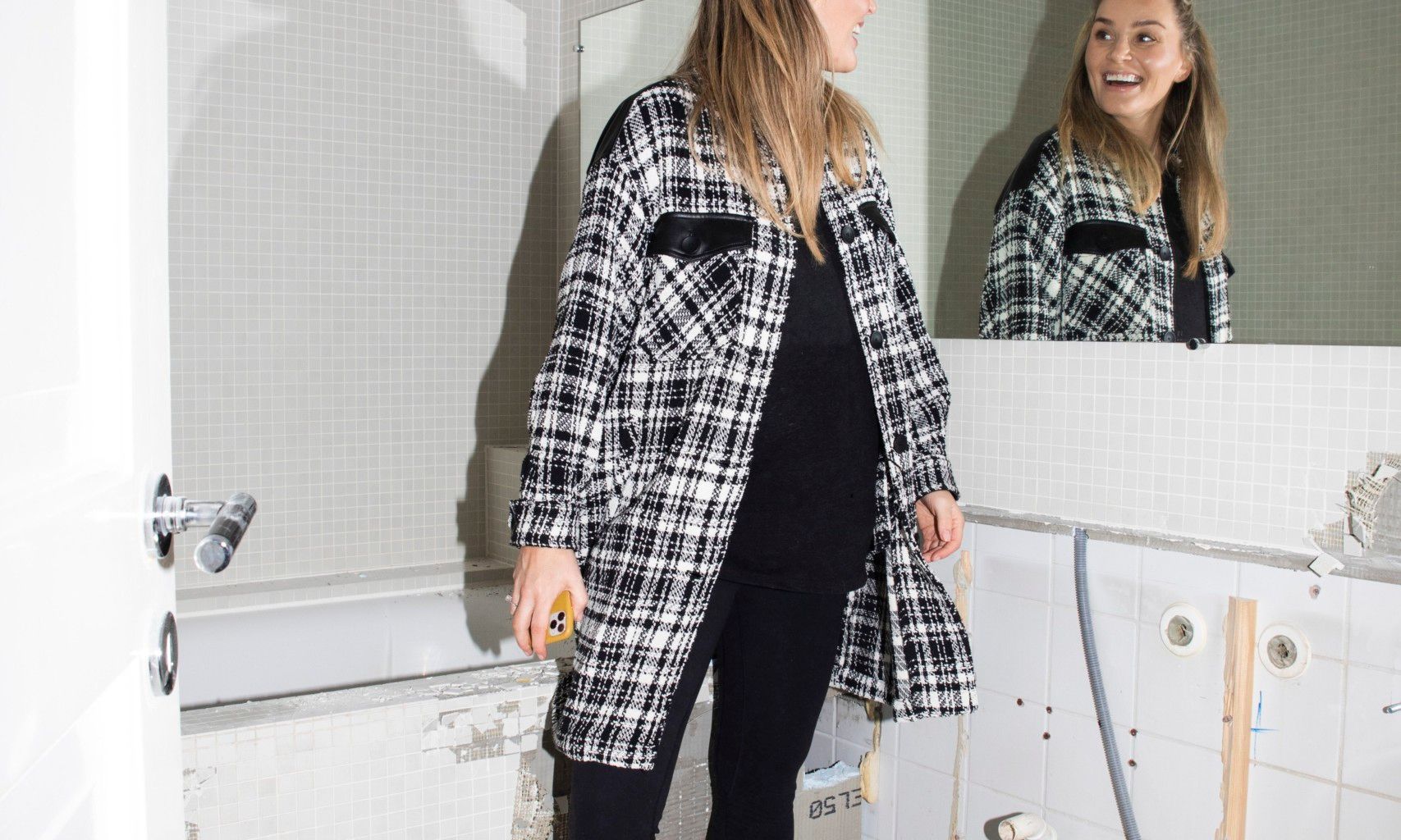 Camilla ler i speilet mens hun står på badet som skal pusses opp.