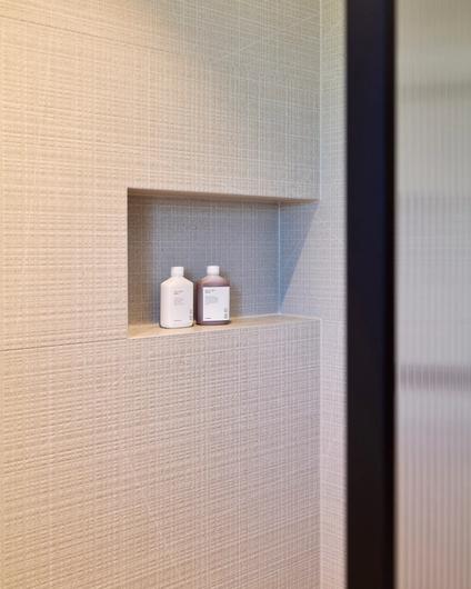 Detaljbilde av dusjsone med dusjnisje og organiske, beige fliser. Utført av Lomundal.