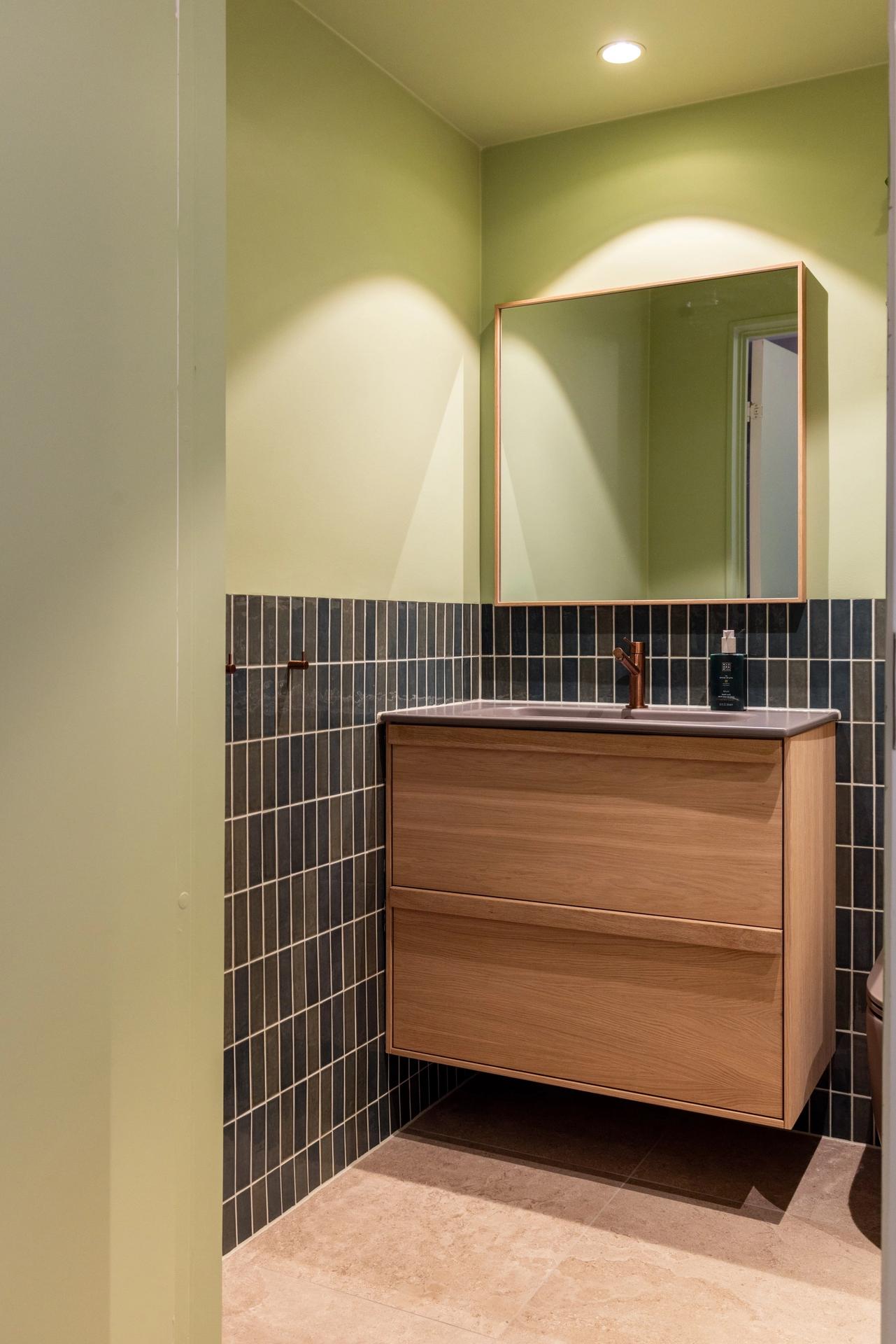 Lyst bad i friske farger. Badet kombinerer beige nyanser med lyst treverk, og vegger i grønntoner. Et moderne, nyoppusset bad med personlig uttrykk. Utført av Lomundal. - Bilde