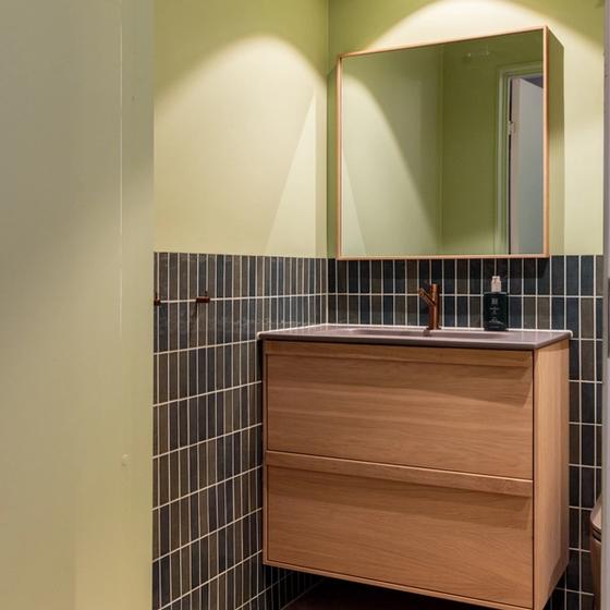 Lyst bad i friske farger. Badet kombinerer beige nyanser med lyst treverk, og vegger i grønntoner. Et moderne, nyoppusset bad med personlig uttrykk. Utført av Lomundal.