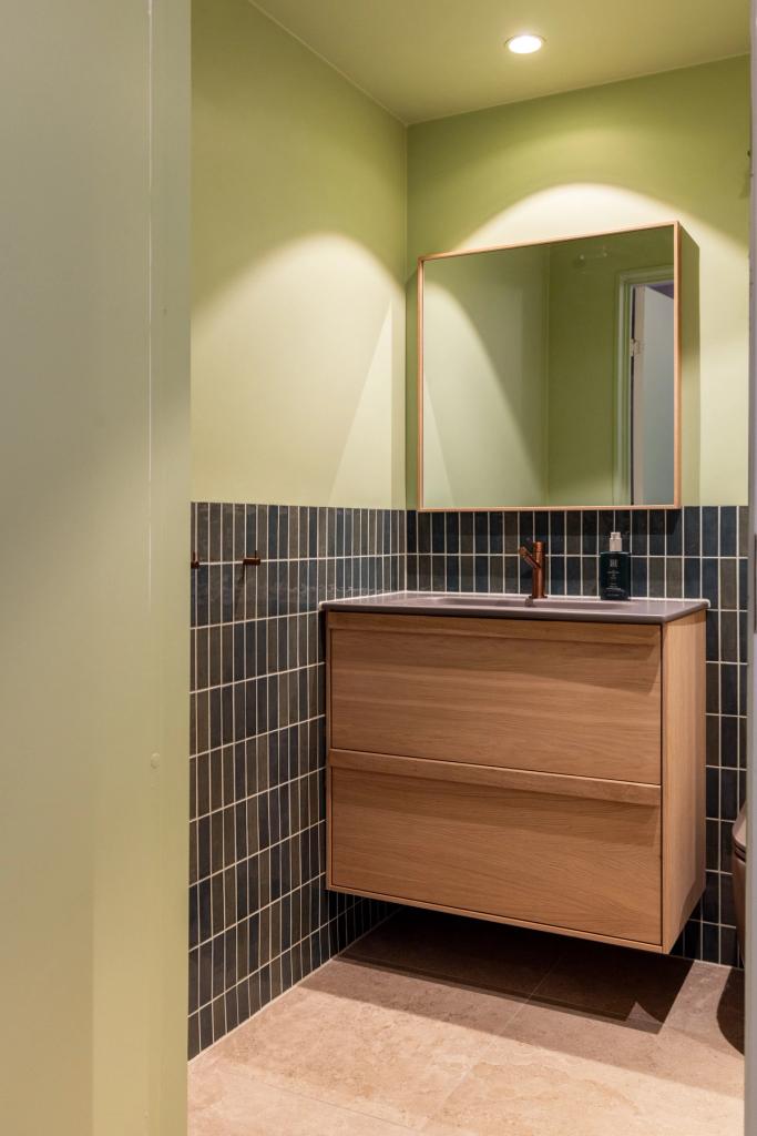 Lyst bad i friske farger. Badet kombinerer beige nyanser med lyst treverk, og vegger i grønntoner. Et moderne, nyoppusset bad med personlig uttrykk. Utført av Lomundal.