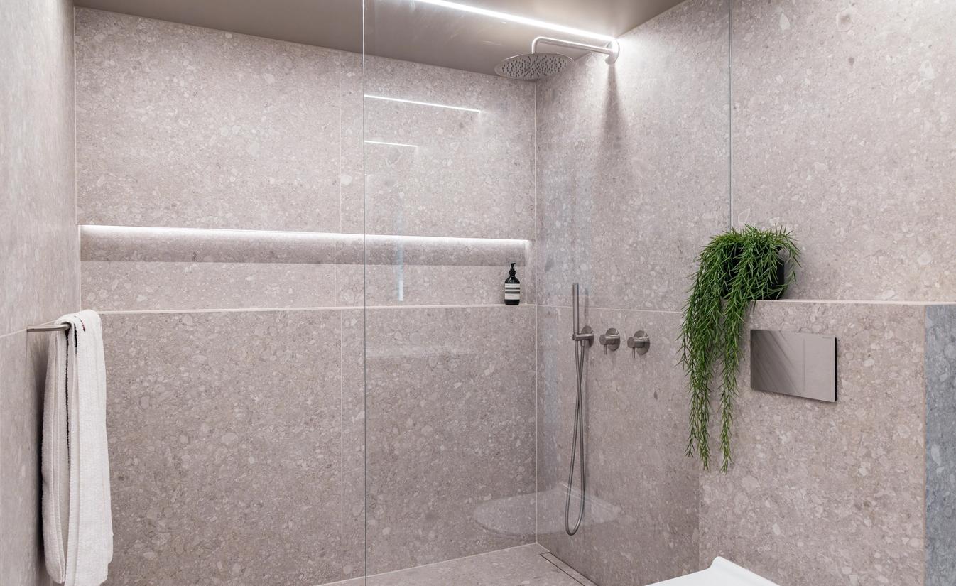 Stort dusjrom med lyse grå fliser fra Fagflis, innebygd hyllenisje med LED-stripe og innebygde armaturer fra Qtoo.