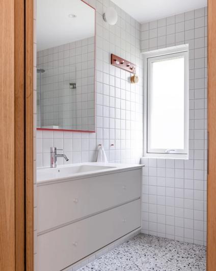 Bad med hvite, kvadratiske veggfliser, terrazzogulv og hvit baderomsinnredning. Utført av Lomundal.