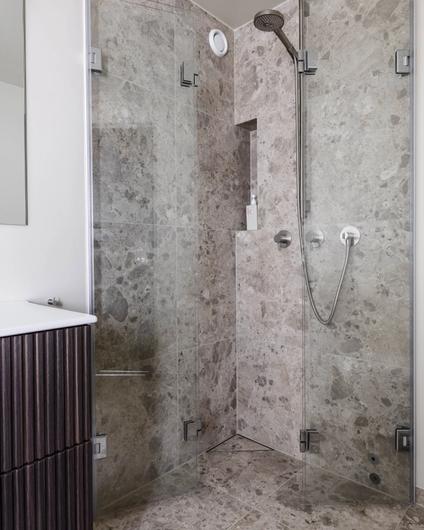 Dusjrom med fliser av stein i beige tone, designsluk i hjørnet og armaturer i børstet krom. Utført av Lomundal.