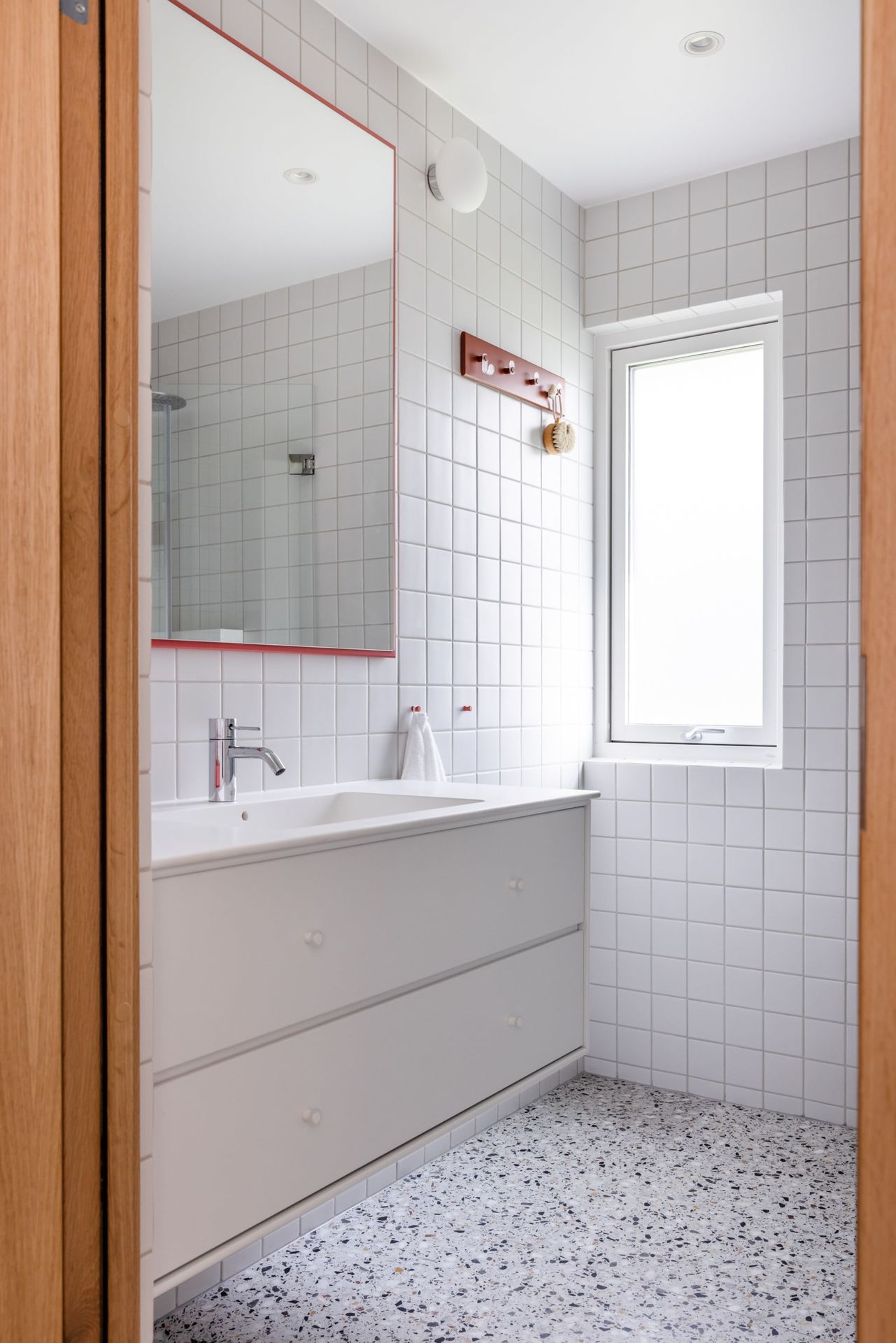 Detaljbilde av retro baderom med hvite fliser på vegg og røde detaljer. Utført av Lomundal. - Bilde