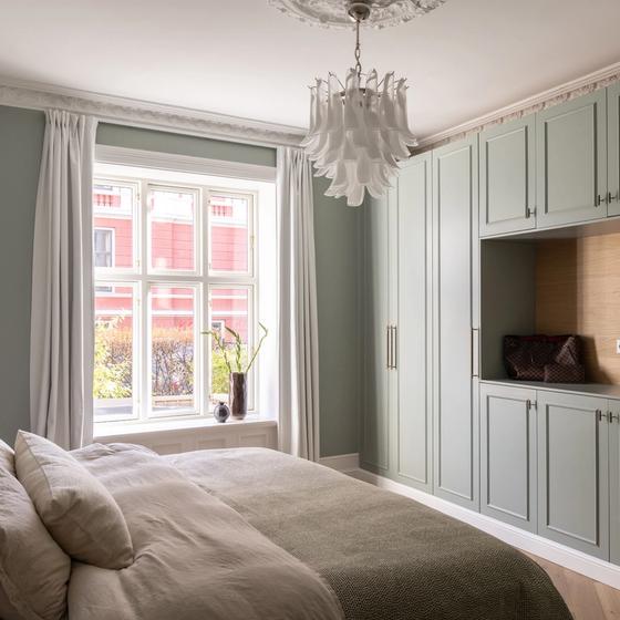 Klassisk soverom i en dus grønnfarge med hvite, elegante stukkaturlister og rosett. Rommet har en behagelig og lys atmosfære, med detaljer i lyst treverk og plassbygd skap. Utført av Lomundal.
