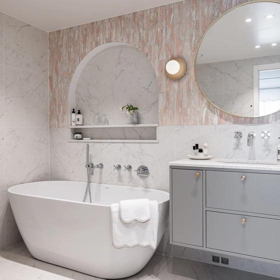 Eksklusivt, klassisk bad i lyse, delikate fargetoner. Badet er flislagt med norsk, rosa Fauske marmor og Carrara marmor. Badet har et frittstående badekar og en buet dusjnisje på vegg. Utført av Lomundal.