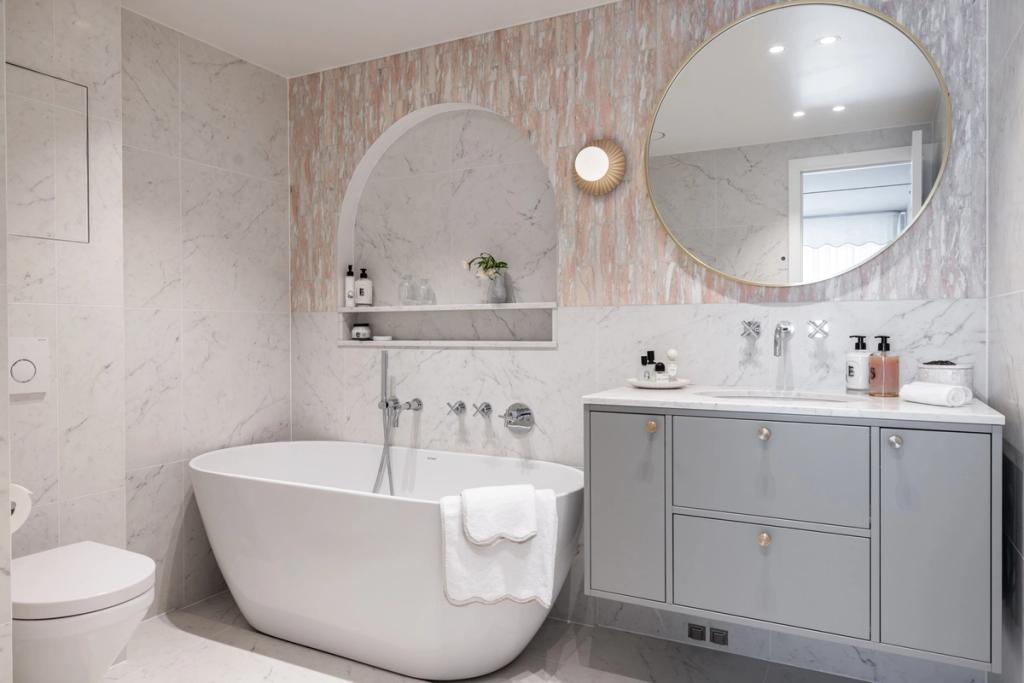 Eksklusivt, klassisk bad i lyse, delikate fargetoner. Badet er flislagt med norsk, rosa Fauske marmor og Carrara marmor. Badet har et frittstående badekar og en buet dusjnisje på vegg. Utført av Lomundal.