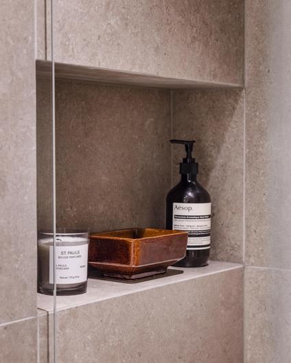 Detaljbilde fra dusjrom med store varme grå fliser og spesialbygget hyllenisje til dusjartikler.