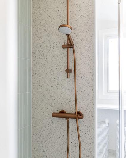 Dusjsone i en nordisk stil med flis med terrazzomønster og blanke, dekorfliser i en mintgrønn farge. Kombinasjonen av ulike materialer og teksturer gir badet et dynamisk uttrykk. Badet er totalrenovert av Lomundal.