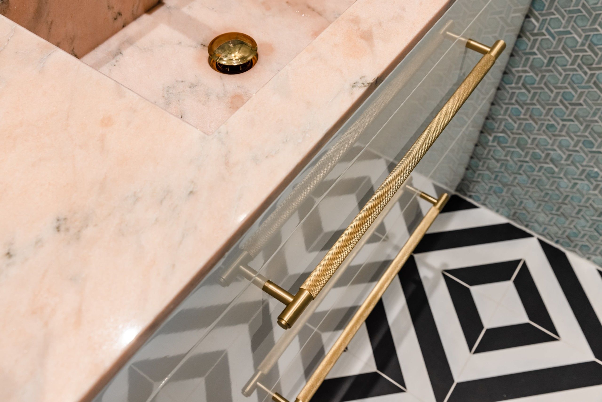 Detaljbilde fra fargerikt bad med blå geometriske fliser på vegg, sorte og hvite geometriske fliser på gulv og baderomsmøbel med rosa benkeplate og detaljer i messing.