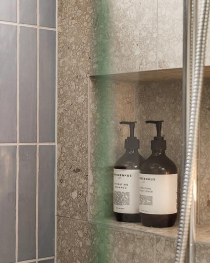 Dusjsone med blå, blanke fliser og terrazzo på vegg, med en liten dusjnisje til oppbevaring av dusjartikler. Badet er totalrenovert av Lomundal.