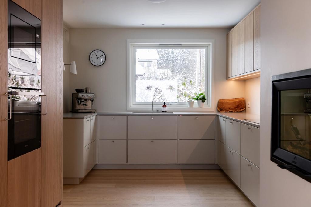 Kjøkkeninnredning med glatte overflater i beigetoner og eikefinér.