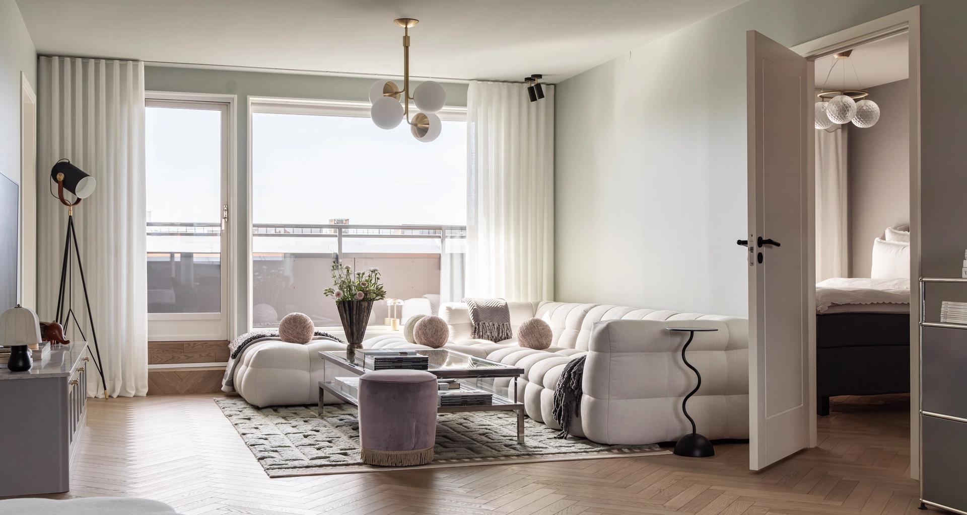Moderne stue med innredning i lyse toner og en vegger i en dempet mintgrønn tone. Gulvet er en lys eikeparkett med fiskebensmønster. Utført av Lomundal.