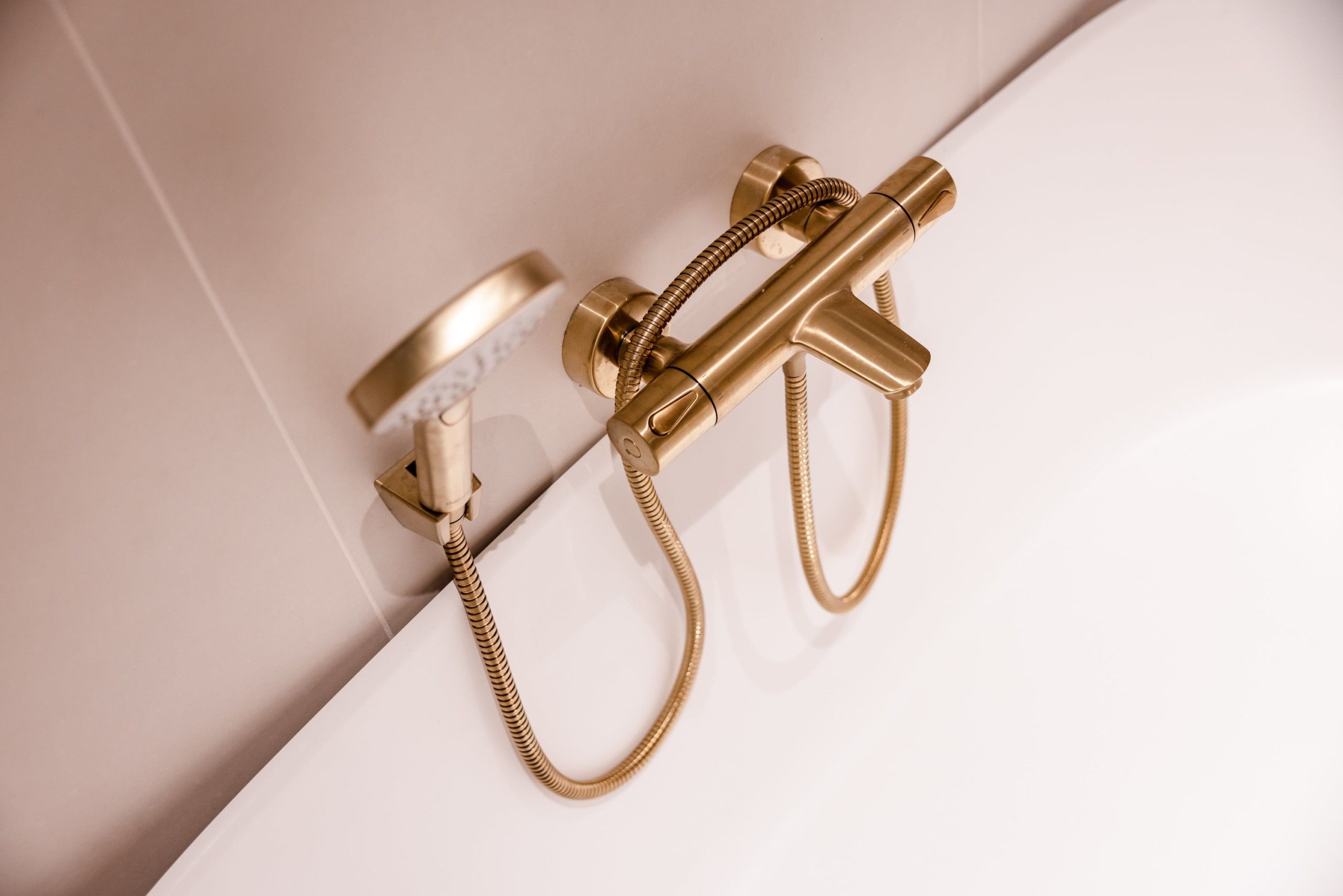 Detaljbilde av armatur i messing over frittstående badekar. Fliser i en varm beige tone. Badet er totalrenovert av Lomundal.