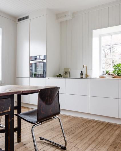 Lyst kjøkken fra Uniform med armatur i messing. Spisebord og stoler bryter opp og skaper fin kontrast mellom nytt og gammelt. Pusset opp av Lomundal.