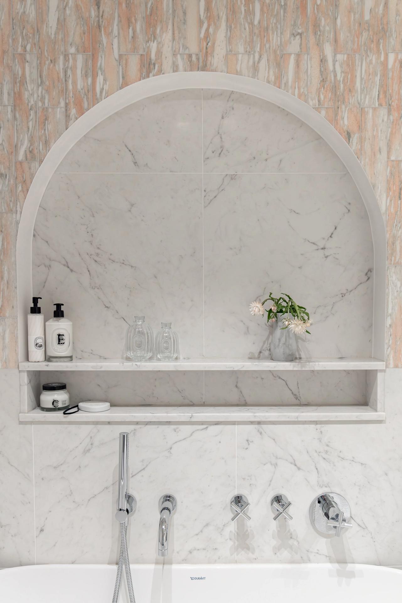 Eksklusivt, klassisk bad i lyse, delikate fargetoner. Badet er flislagt med norsk, rosa Fauske marmor og Carrara marmor. Badet har et frittstående badekar og en buet dusjnisje på vegg. Utført av Lomundal. - Bilde