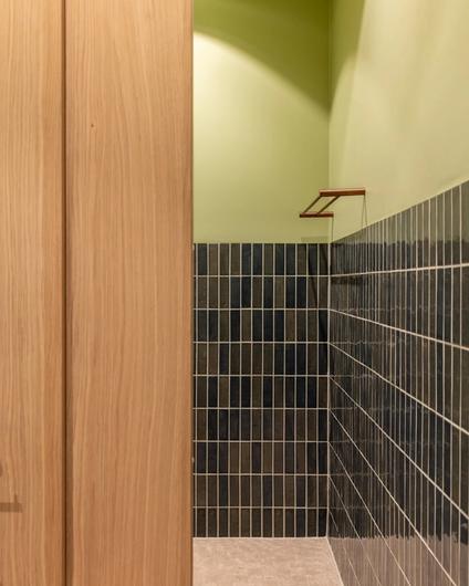 Moderne bad i grønntoner med en romslig dusjsone. På gulvet er det små kvadratiske beige fliser. På veggen er det smale blanke fliser i en dyp grønnfarge kombinert med malte flater.