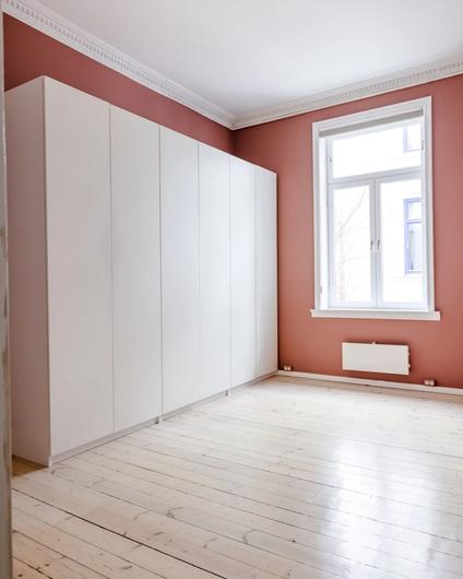 Soverom før oppussing med originalt furugulv, mørke rosa vegger og stukkatur i taket.