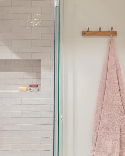 Knagger i tre og hyllenisje i dusjen, med rosa håndkle. Badet er totalrenovert av Lomundal.