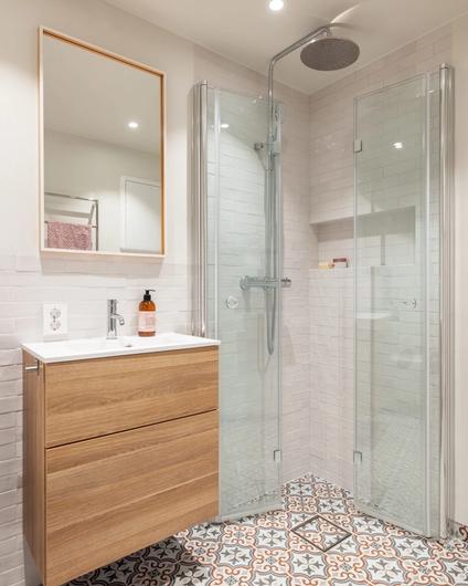 Dusjhjørne i glass med hvite brick-fliser og mønsterflis på gulvet. Badet er totalrenovert av Lomundal.