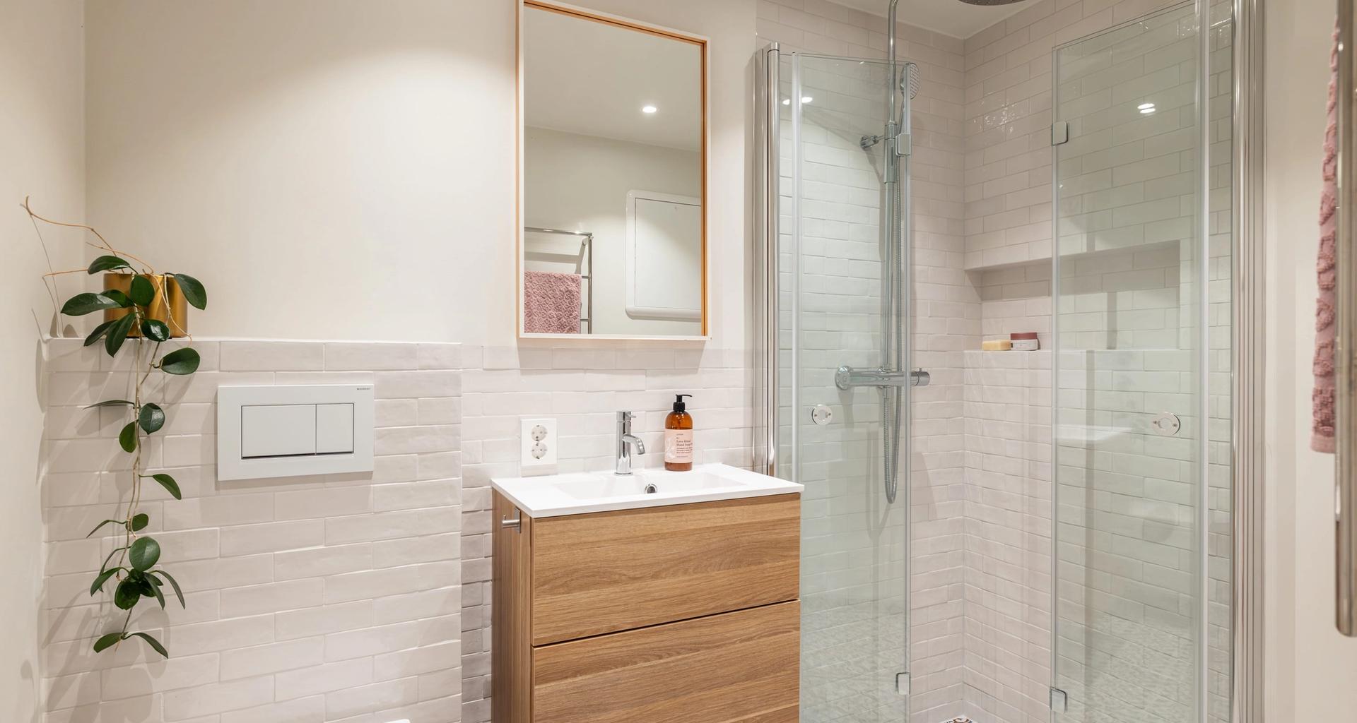 Retrobad med mønsterflis på gulv og hvite brick-fliser på vegg. Baderomsmøbel i tre og dusjhjørne i glass. Badet er totalrenovert av Lomundal.