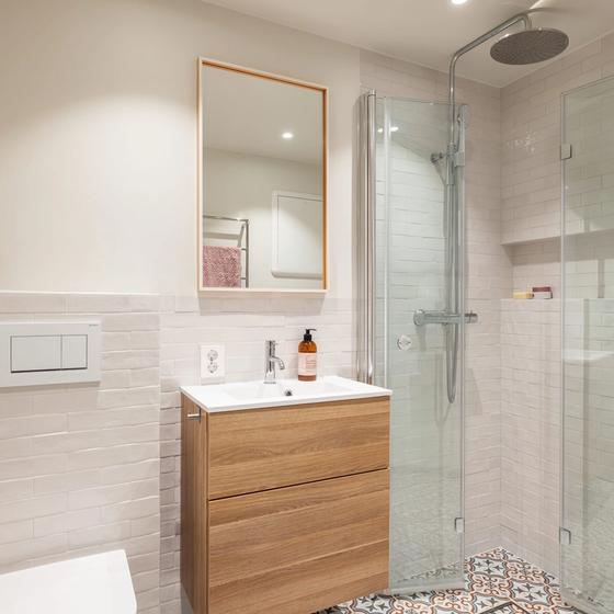 Retrobad med mønsterflis på gulv og hvite brick-fliser på vegg. Baderomsmøbel i tre og dusjhjørne i glass. Badet er totalrenovert av Lomundal.