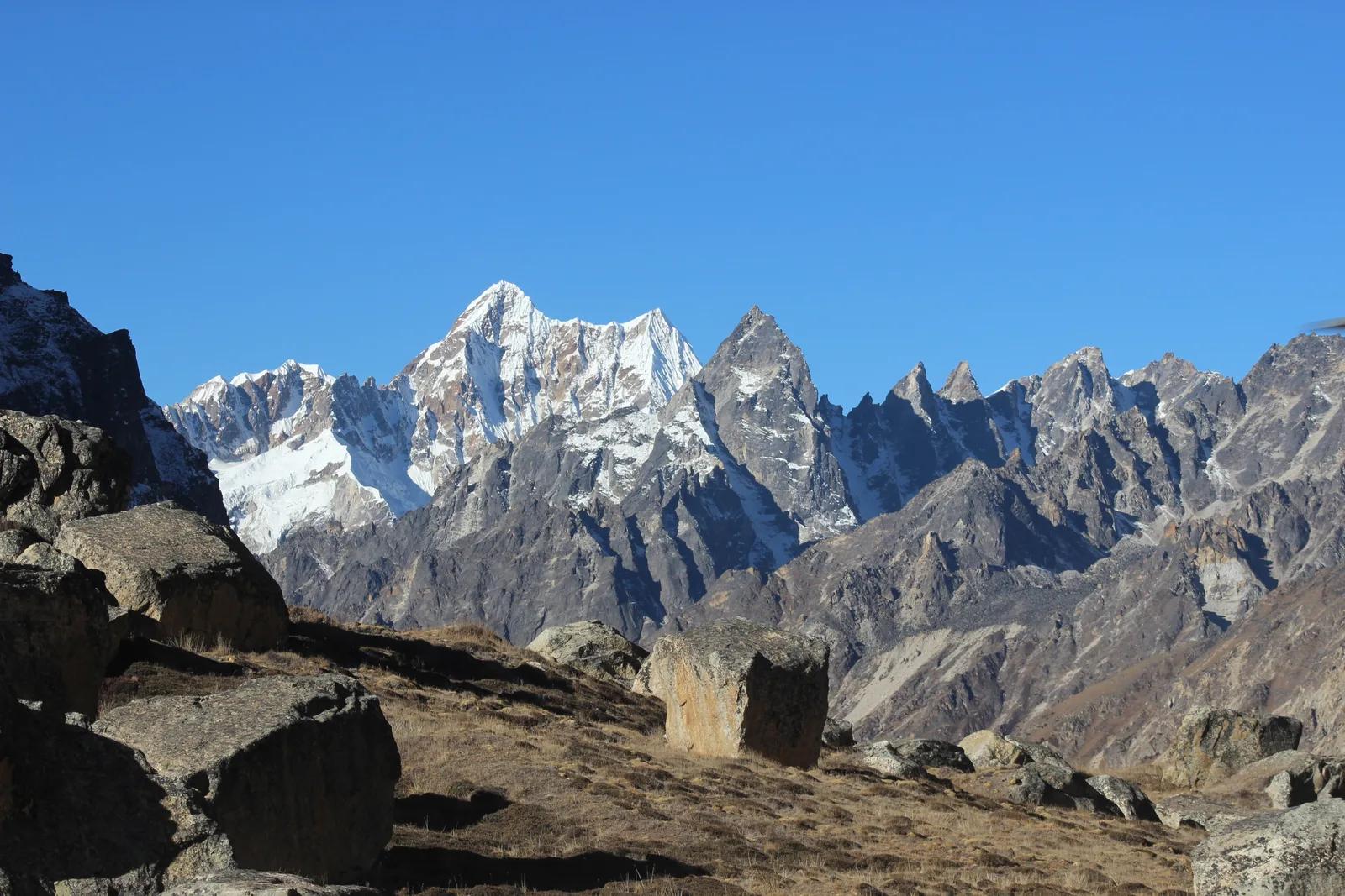 Boulders and dry alpine grass in the upper Ghunsa valley on the Kanchenjunga trek, below a line of rock and snow peaks under a clear October sky