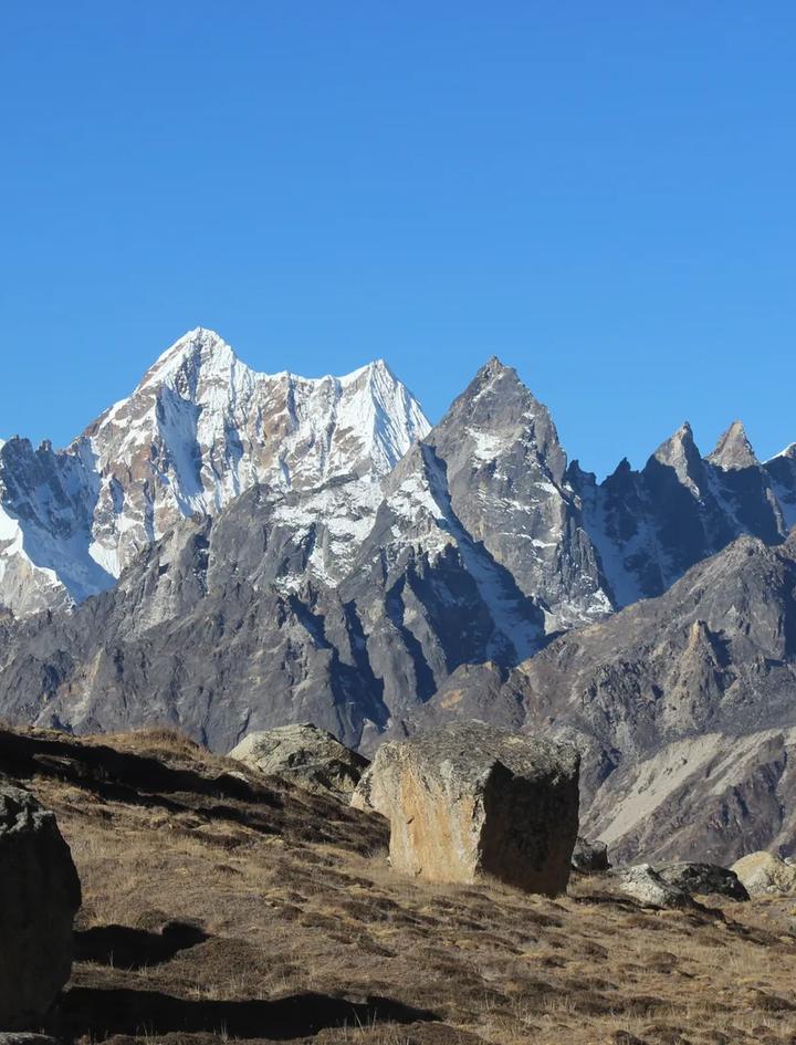 Boulders and dry alpine grass in the upper Ghunsa valley on the Kanchenjunga trek, below a line of rock and snow peaks under a clear October sky