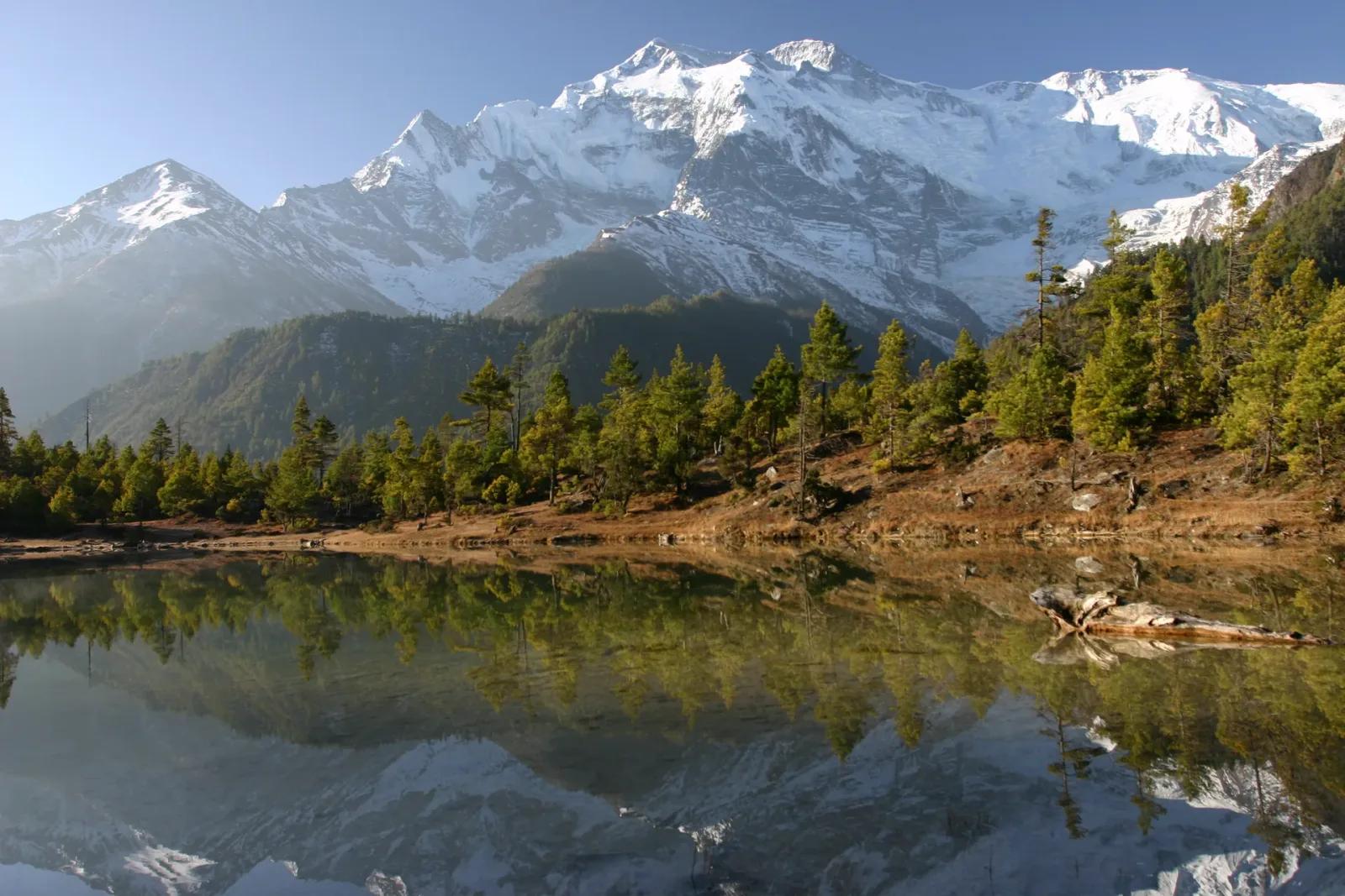 Snow-capped Annapurna peaks reflected in a still lake above the Marsyangdi valley, the region the Manaslu Circuit drops into after crossing Larkya La