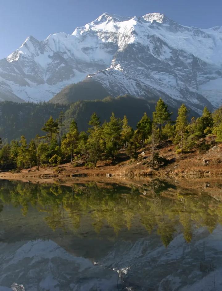 Snow-capped Annapurna peaks reflected in a still lake above the Marsyangdi valley, the region the Manaslu Circuit drops into after crossing Larkya La