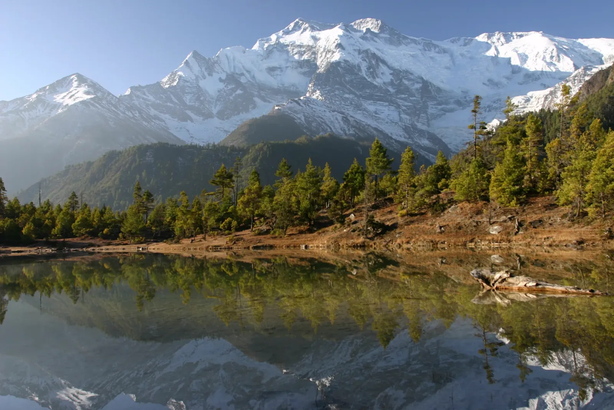 Snow-capped Annapurna peaks reflected in a still lake above the Marsyangdi valley, the region the Manaslu Circuit drops into after crossing Larkya La