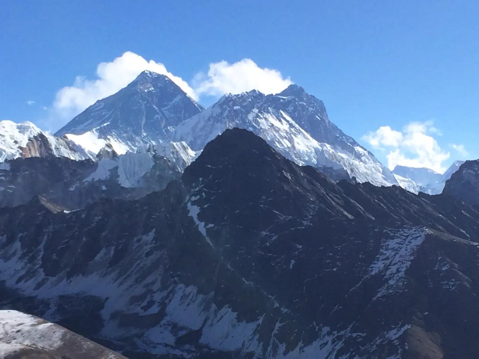 The summit pyramid of Everest and the long wall of Lhotse rising above a dark ridgeline, seen across the valley on a clear morning