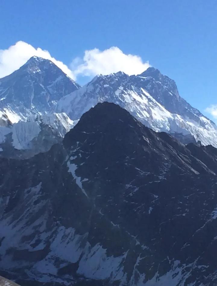 The summit pyramid of Everest and the long wall of Lhotse rising above a dark ridgeline, seen across the valley on a clear morning