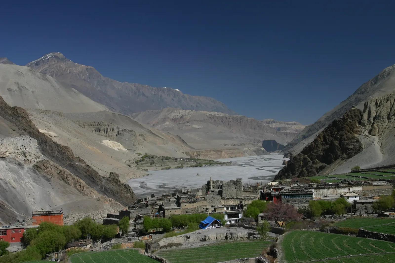 A stone-built village at the mouth of a wide river valley in the Nepal Himalaya, the kind of gateway settlement where restricted-area trekking permits are checked