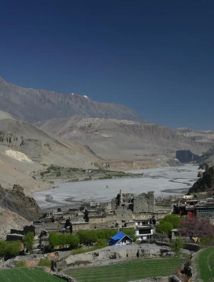 A stone-built village at the mouth of a wide river valley in the Nepal Himalaya, the kind of gateway settlement where restricted-area trekking permits are checked