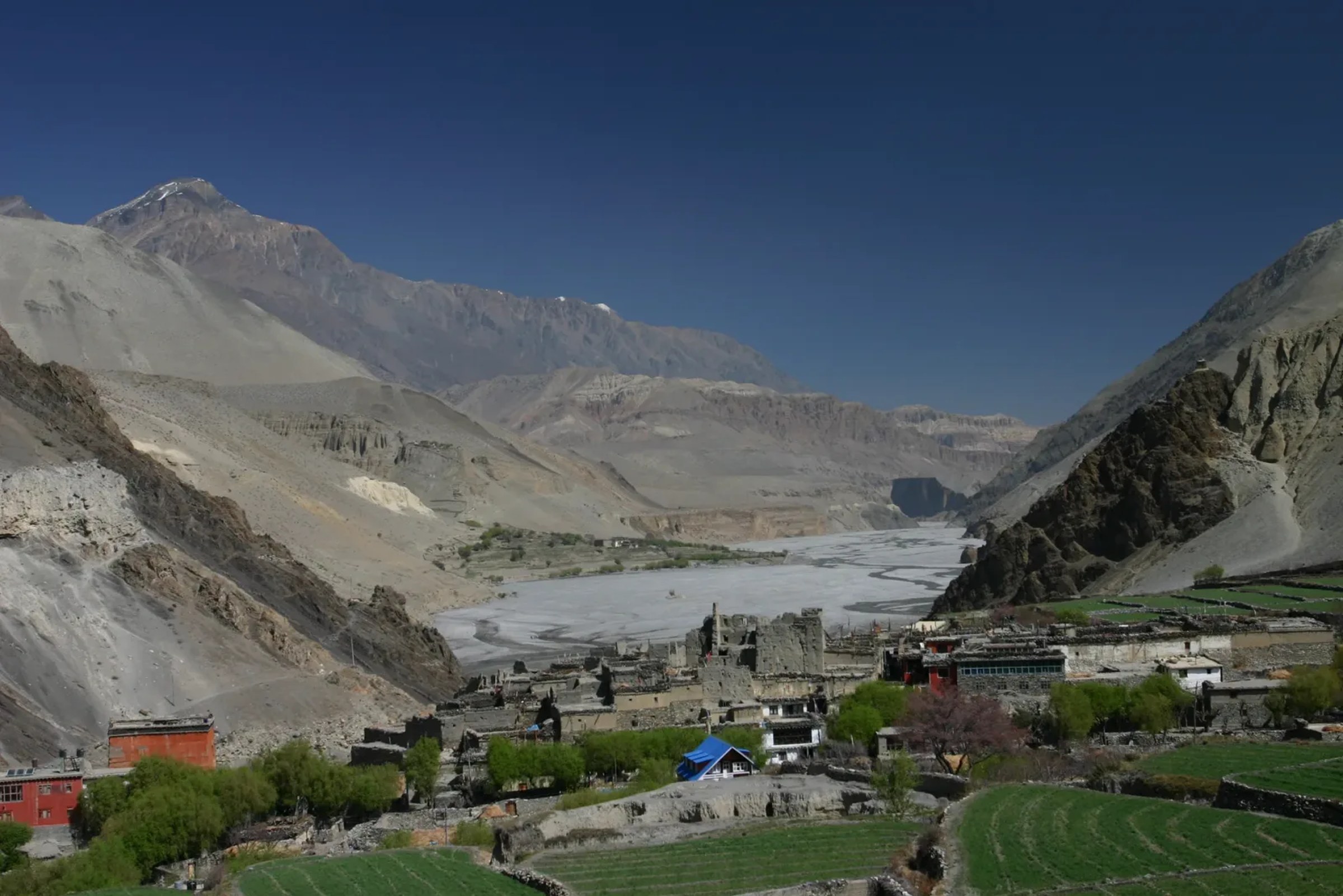 A stone-built village at the mouth of a wide river valley in the Nepal Himalaya, the kind of gateway settlement where restricted-area trekking permits are checked