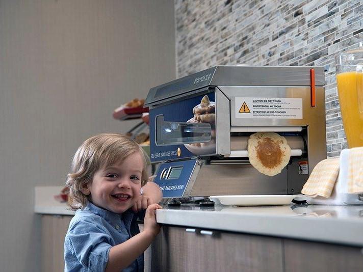 Lachende peuter bij de pancake machine, met een verse pancake die eruit rolt