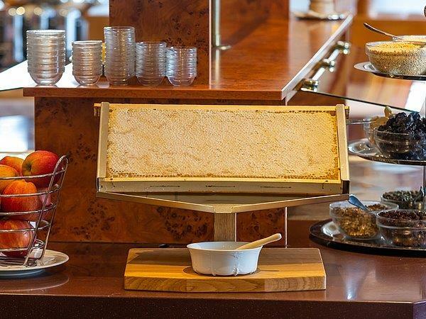 Honingraat in een roestvrijstalen display op het ontbijtbuffet, naast schaaltjes met noten en fruit
