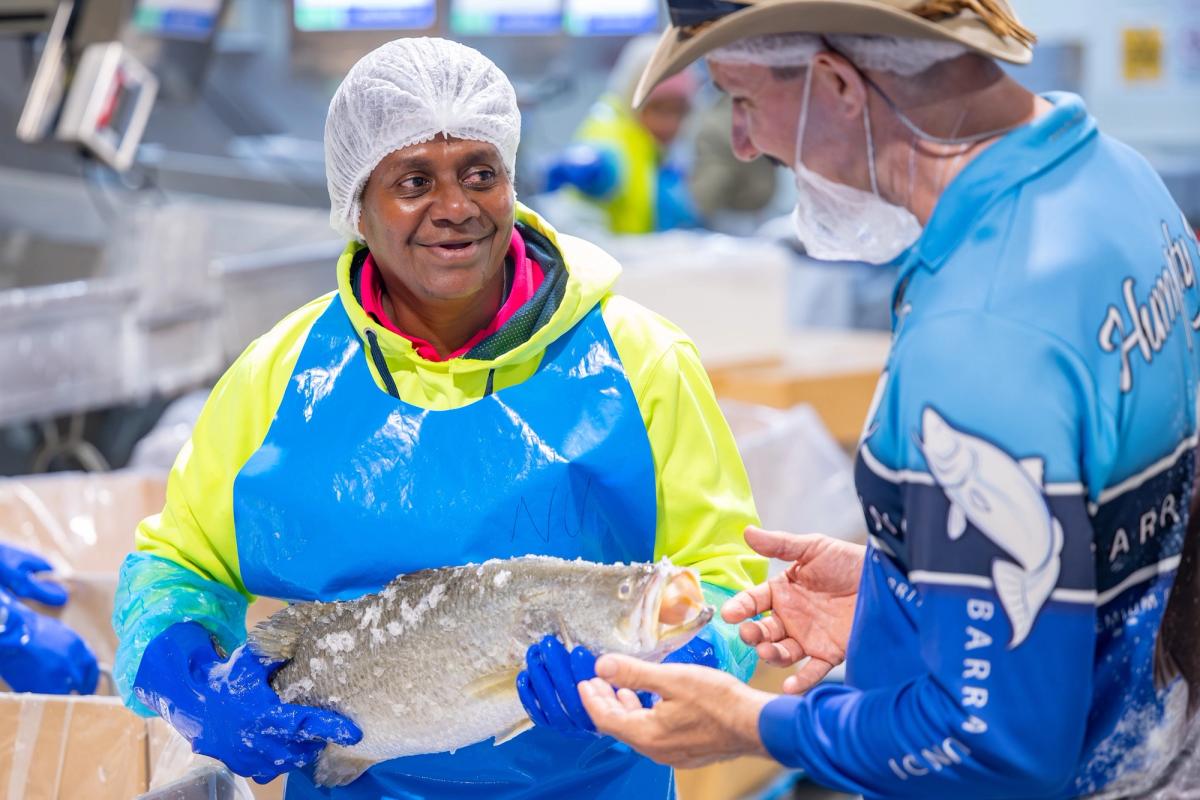 Smiling worker in hairnet and hi-vis apron on the processing floor at Humpty Doo Barramundi, with a colleague in company jersey.