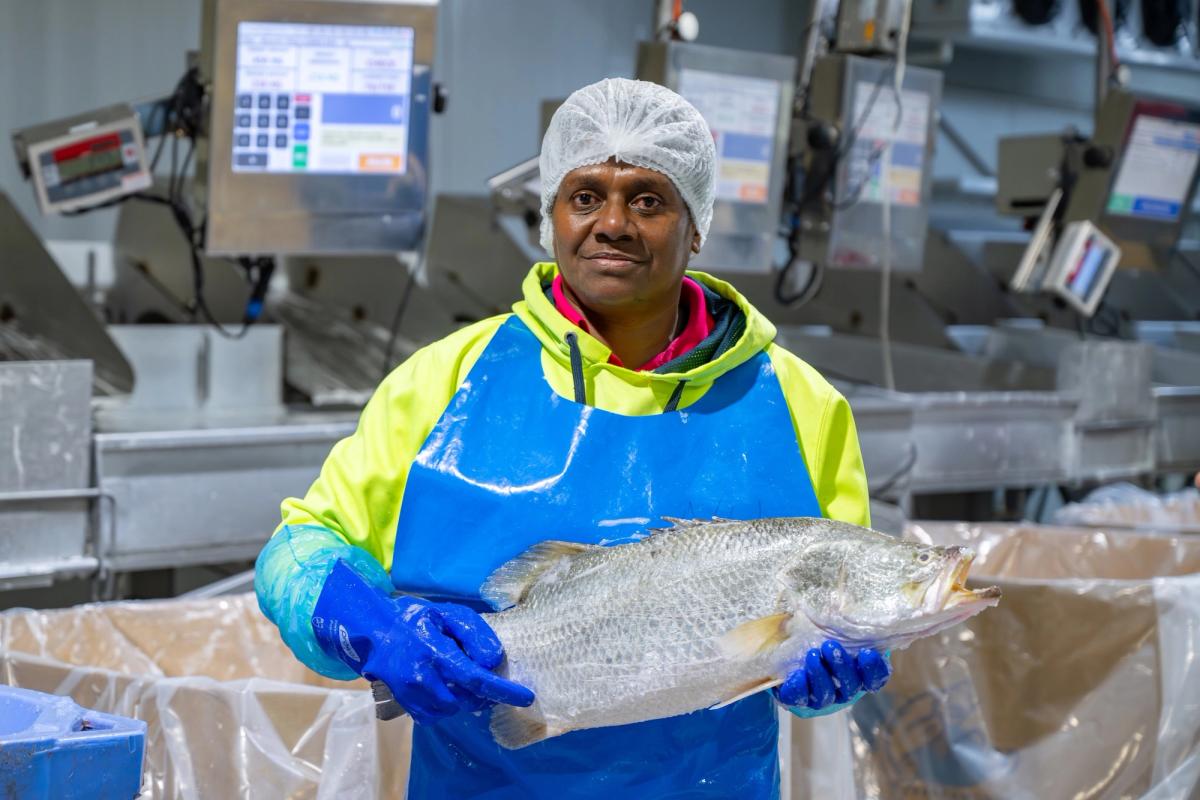 Humpty Doo Barramundi processing worker holding a freshly processed whole barramundi at a weighing station.