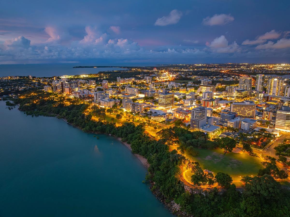 Aerial view of Darwin CBD lit up at night, with the Timor Sea on the left and city lights across the tropical landscape, Northern Territory.