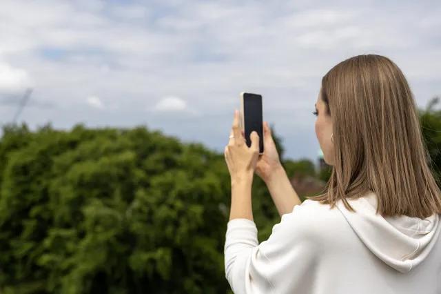 A woman holding a phone to take a photo of some trees