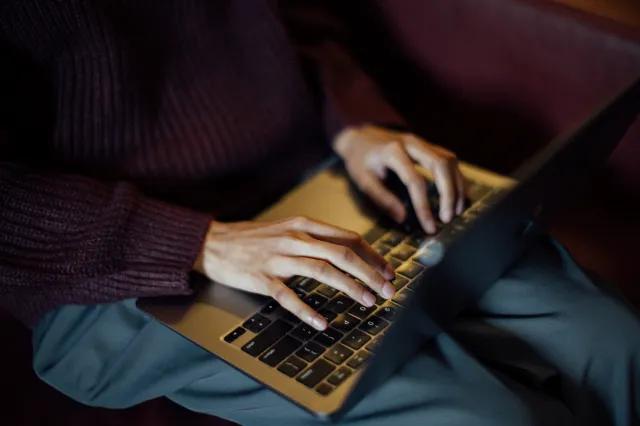 A person typing on a laptop with only their hands and lower torso in shot.